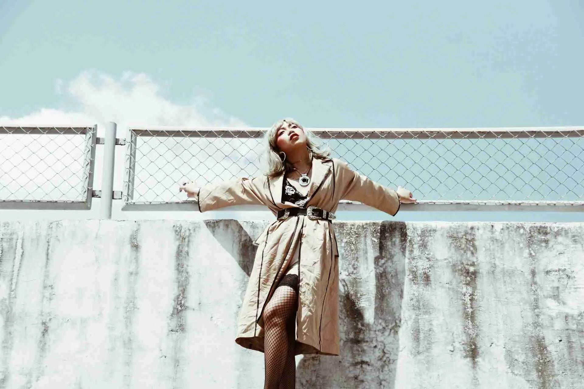 An elegant Asian woman standing against a bright blue sky, symbolizing professionalism and poise, aligning with strategies for managing an online reputation as a luxury escort, as detailed in the blog post.